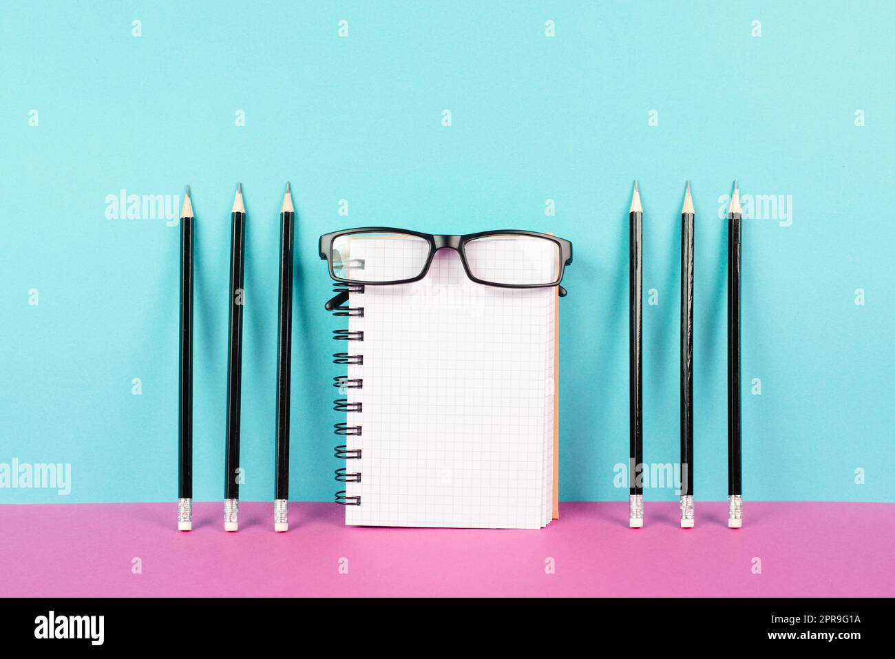 Leeres Notizbuch mit Bleistiften und Brillen auf rosa und blauem Hintergrund, Brainstorming für neue Ideen, Schreiben einer Nachricht, Schreibtisch im Home Office Stockfoto