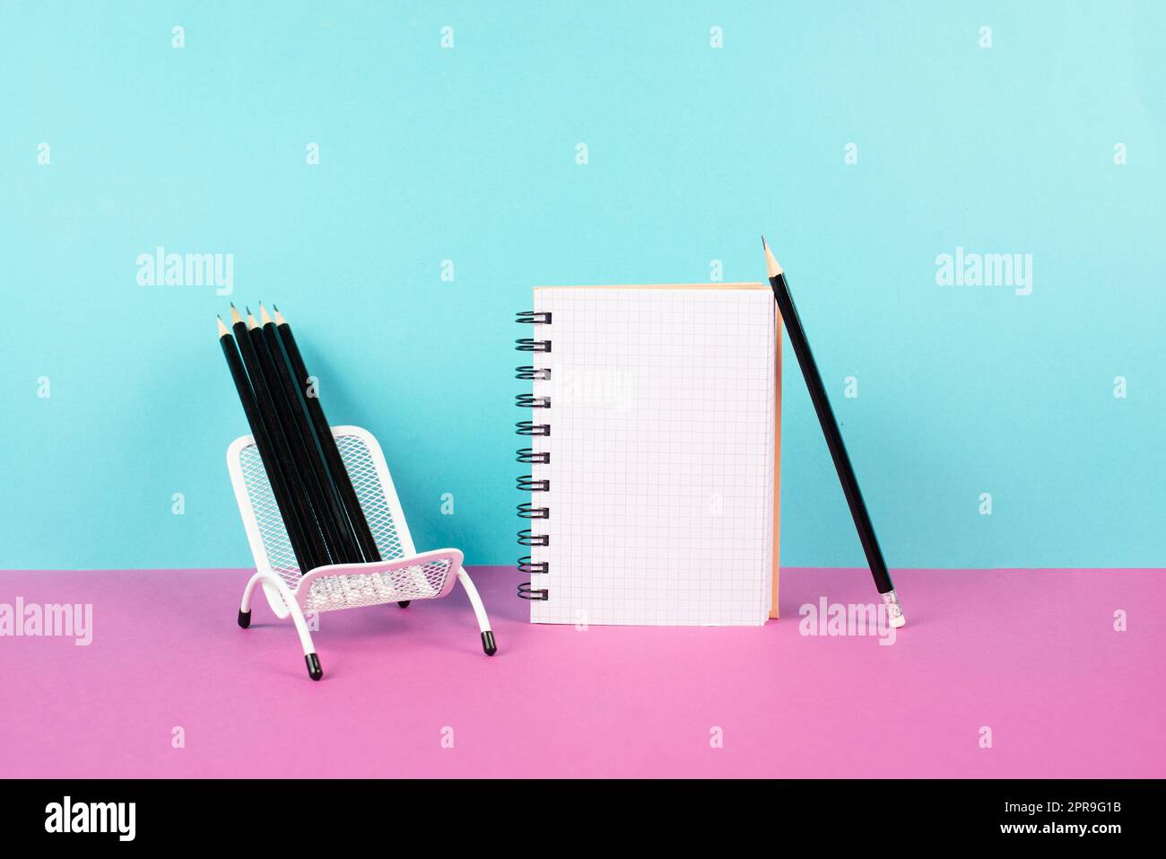 Leeres Notizbuch mit Bleistiften in einem Stuhl, kreativ sein und Brainstorming für neue Ideen durchführen, eine Nachricht schreiben, Arbeitsbereich, rosa und türkisfarbener Hintergrund Stockfoto