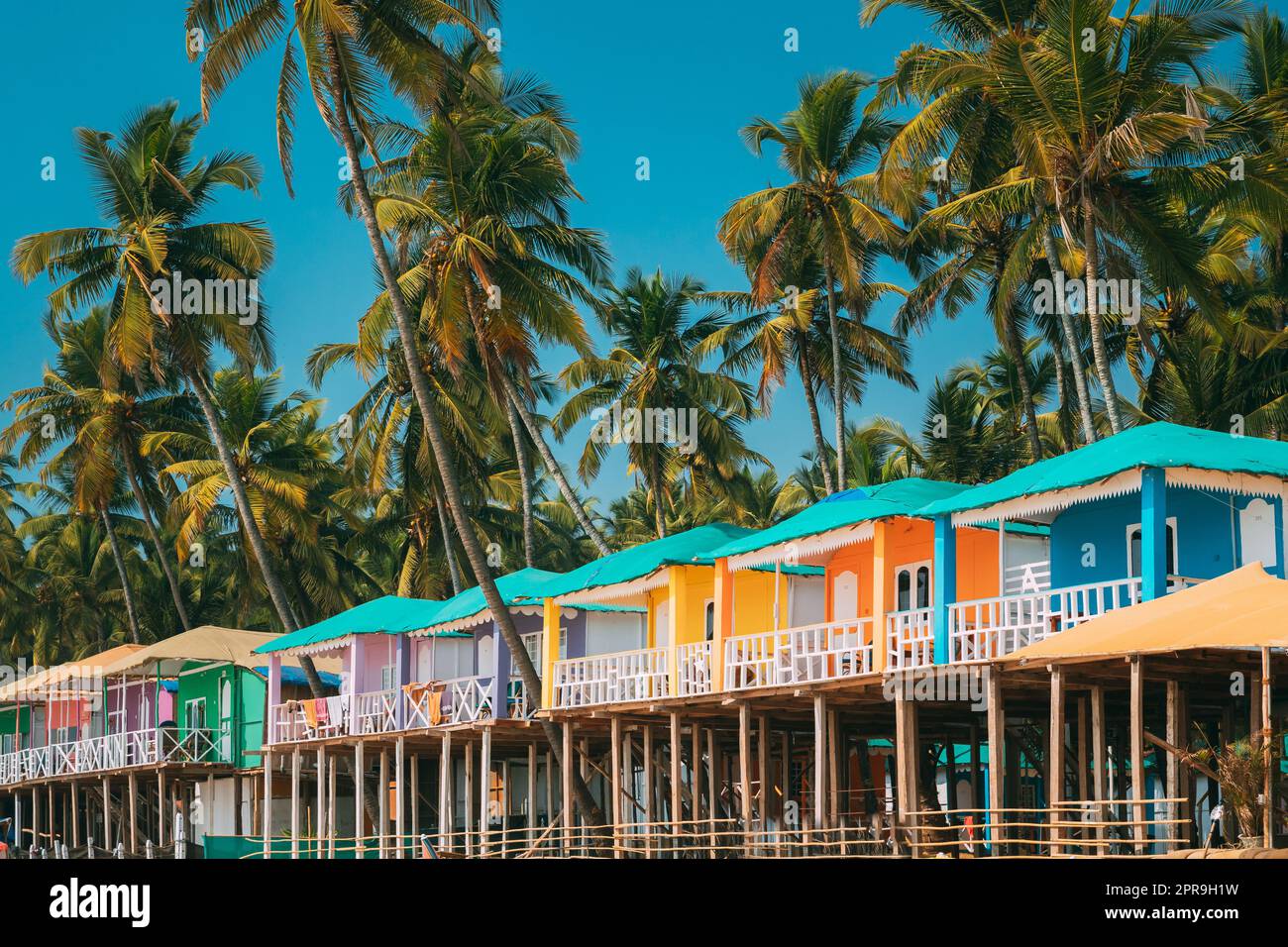 Canacona, Goa, Indien. Berühmte gemalte Gästehäuser am Strand von п vor dem Hintergrund hoher Palmen in Sonnentag Stockfoto