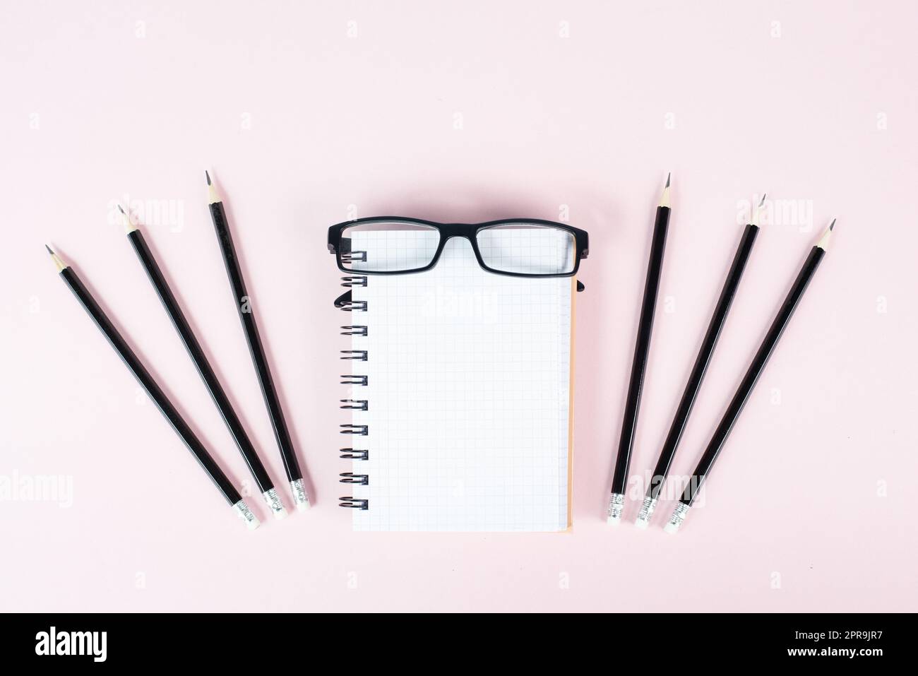 Leeres Notizbuch mit Bleistiften und Brillen auf rosafarbenem Hintergrund, Brainstorming für neue Ideen, Schreiben einer Botschaft, Schreibtisch im Home Office Stockfoto