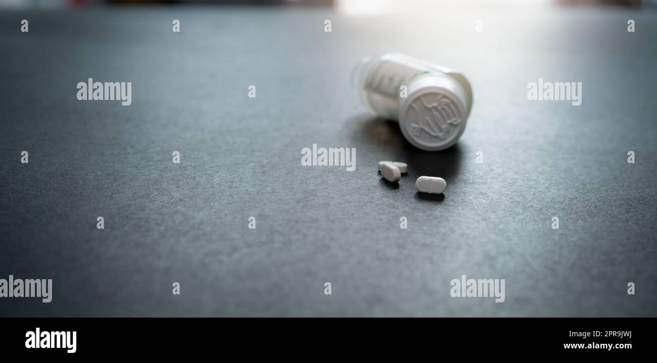 Weiße Tabletten Tabletten und verwischt kindergesicherte Pillenflasche auf schwarzem Tisch. Verschreibungspflichtige Medikamente. Pharmazeutische Industrie. Medizinische Versorgung. Medikamente zur Heilung von Krankheiten. Pharmazeutisches Produkt. Kleine weiße Tabletten. Stockfoto