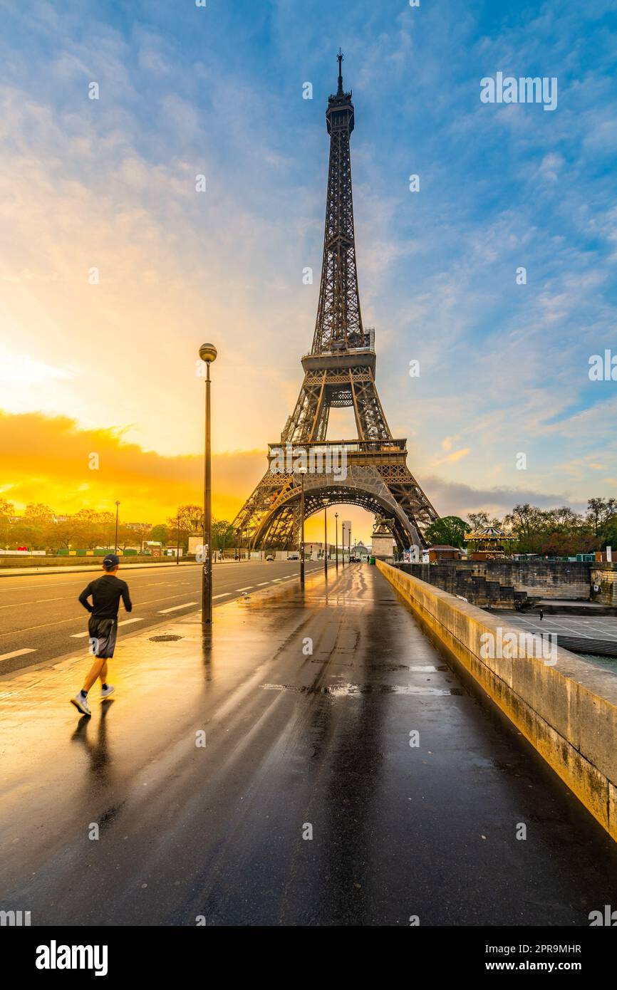 Junger Mann rennt nach Regen bei Sonnenaufgang auf der Brücke. Joggen am Morgen unter dem Eiffelturm in Paris, Frankreich Stockfoto