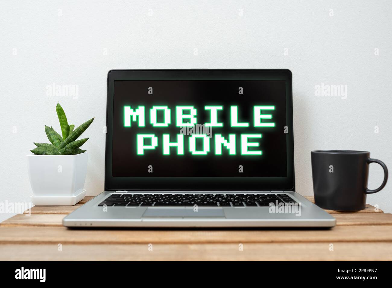 Schreiben mit Anzeige von Text Mobiltelefon. Internetkonzept Ein Handheld-Gerät, mit dem Anrufe und Nachrichten empfangen werden können Laptop mit wichtigen Informationen auf dem Tisch mit Pflanzen und einer Tasse Kaffee. Stockfoto