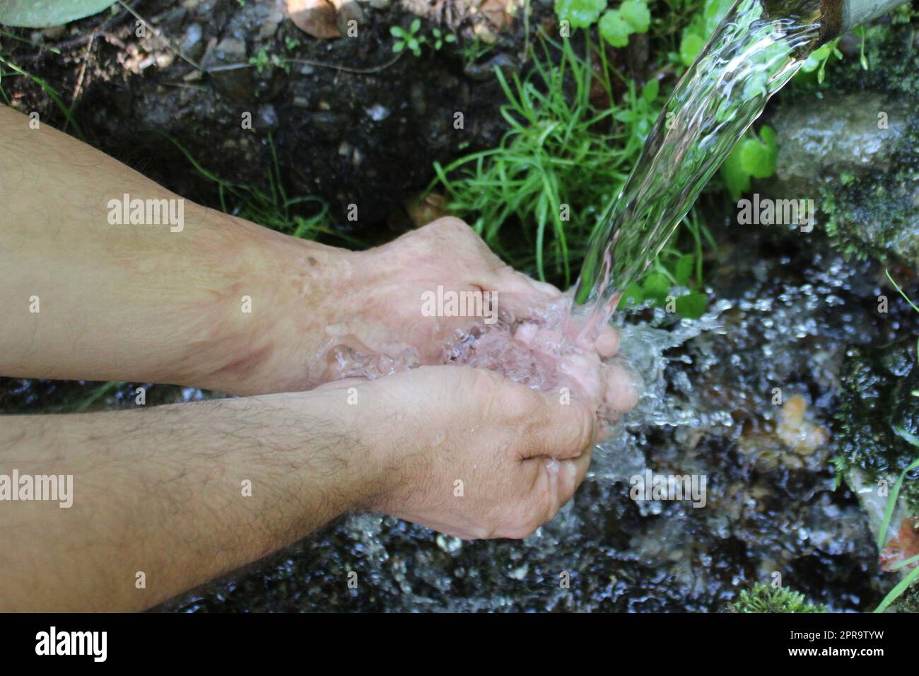 Ein Mann wäscht sich an einer Quelle im Wald die Hände. Unscharfer natürlicher Hintergrund Stockfoto