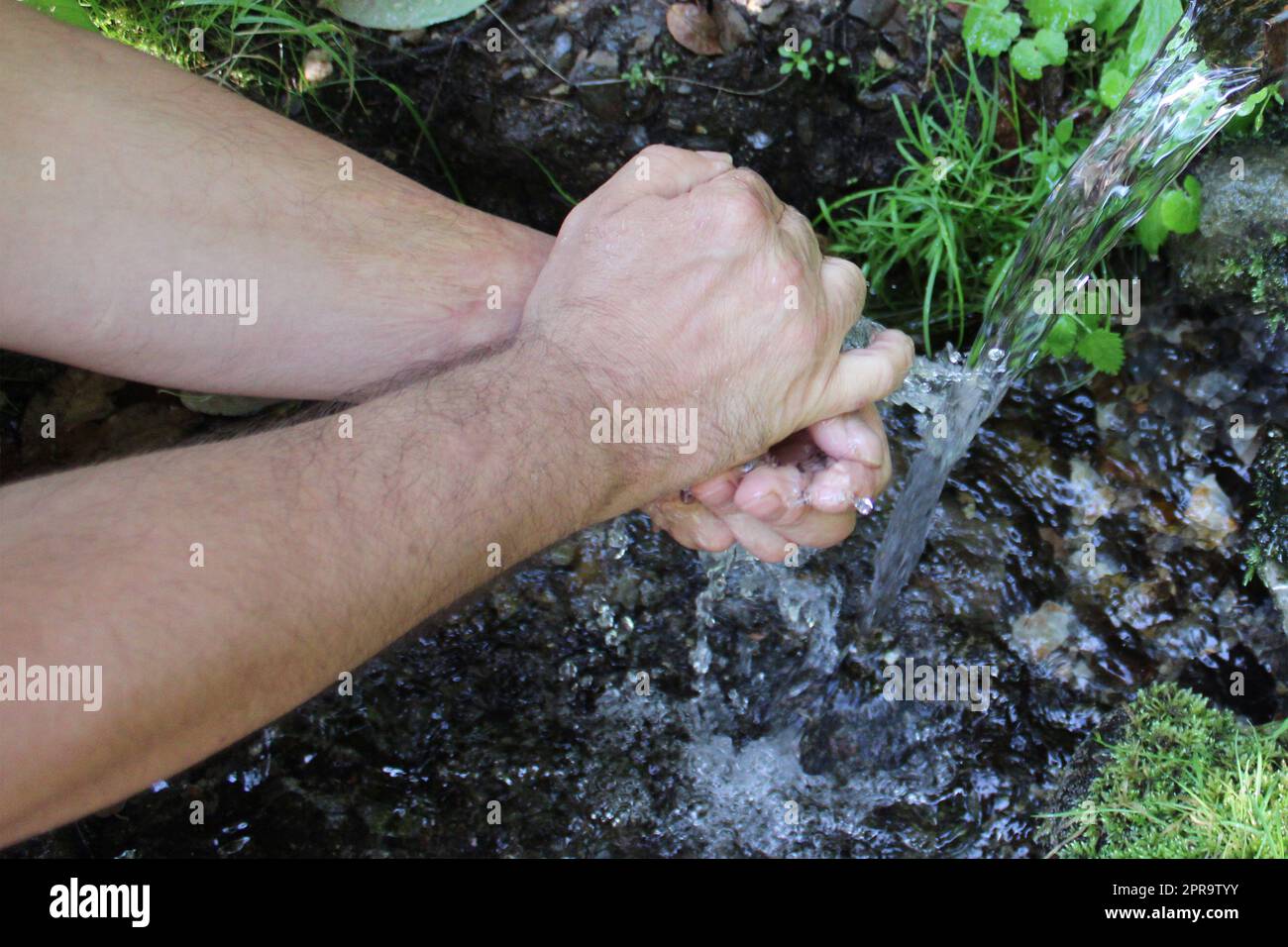 Ein Mann wäscht sich an einer Quelle im Wald die Hände. Unscharfer natürlicher Hintergrund Stockfoto