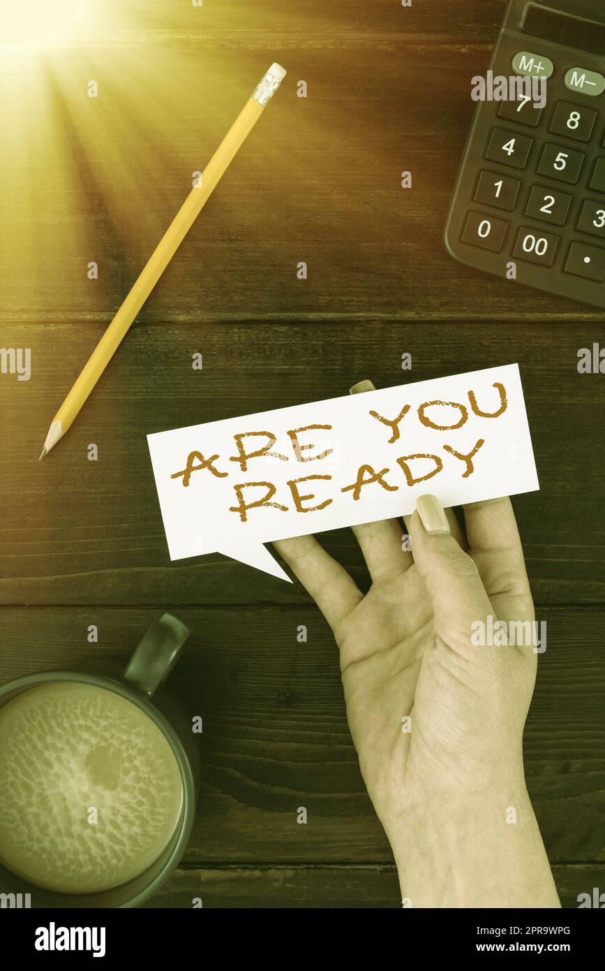 Handschriftlicher Text Are You Ready. Internet-Konzept Wachsamkeit Vorbereitung Dringlichkeitsspiel Beeilen Sie sich, Wide Awake Woman Hand mit Thought Bubble Paper mit Kaffee und Schreibwaren über Holz. Stockfoto