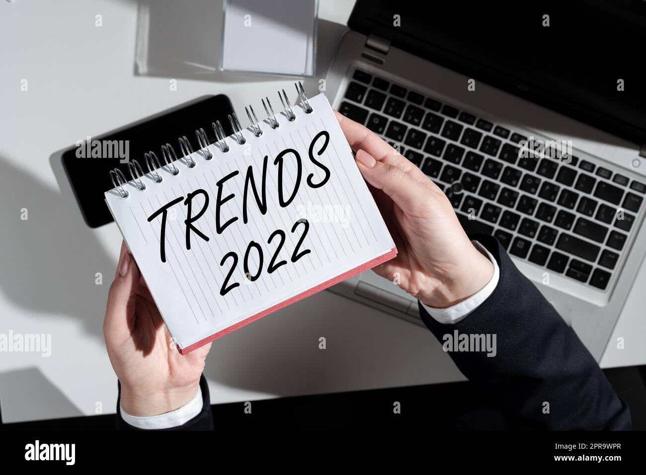 Textbeschriftung zur Darstellung von Trends 2022. Geschäftsidee im kommenden Jahr vorherrschende Tendenz breit diskutiert Online-Geschäftsfrau, die Notebook über Schreibtisch mit Notizen, Mobiltelefon und Laptops hält. Stockfoto