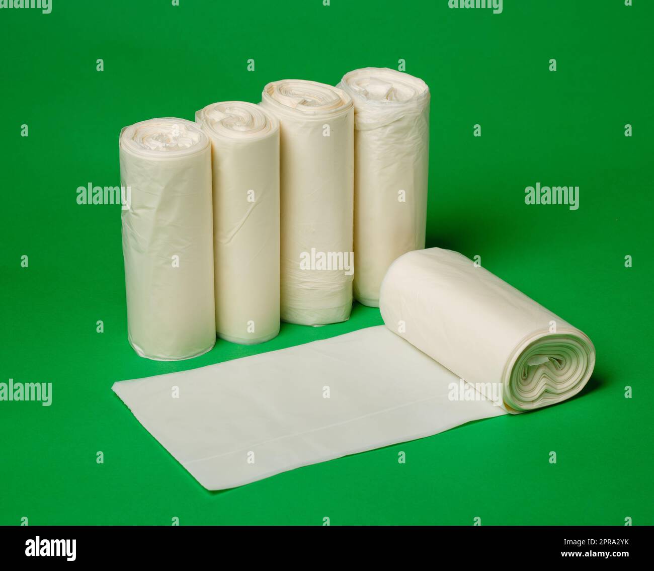 Fünf Rollen biologisch abbaubarer weißer Abfallbeutel aus umweltfreundlichem Kunststoff auf grünem Hintergrund. Stockfoto
