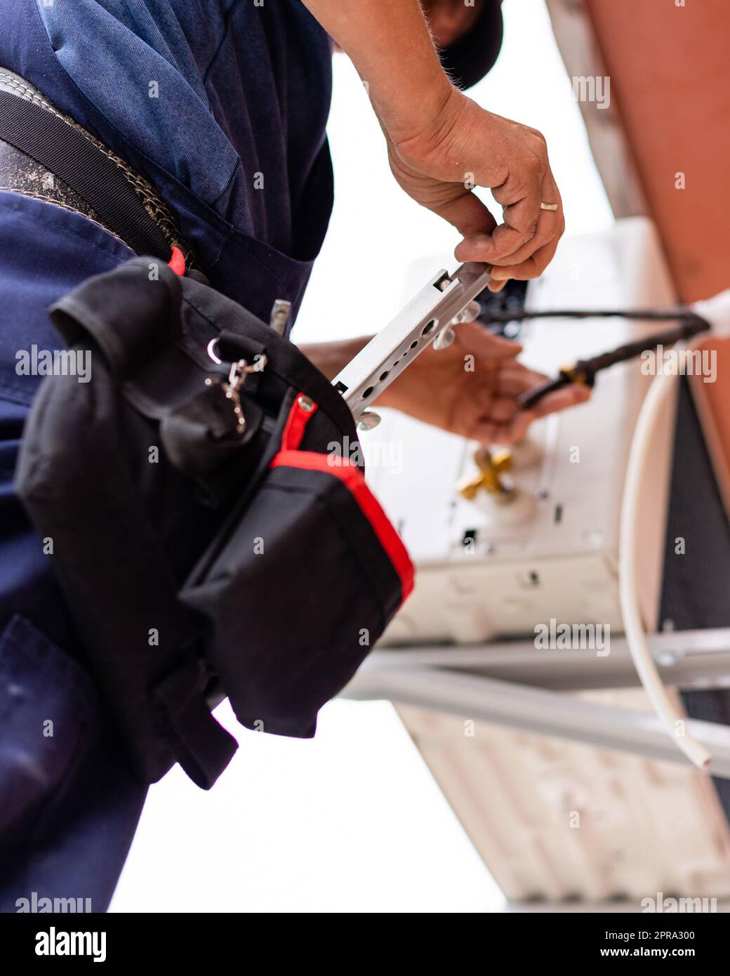 Männlicher Techniker verbindet die Klimaanlage im Freien mit der Wand des alten Wohngebäudes. Stockfoto