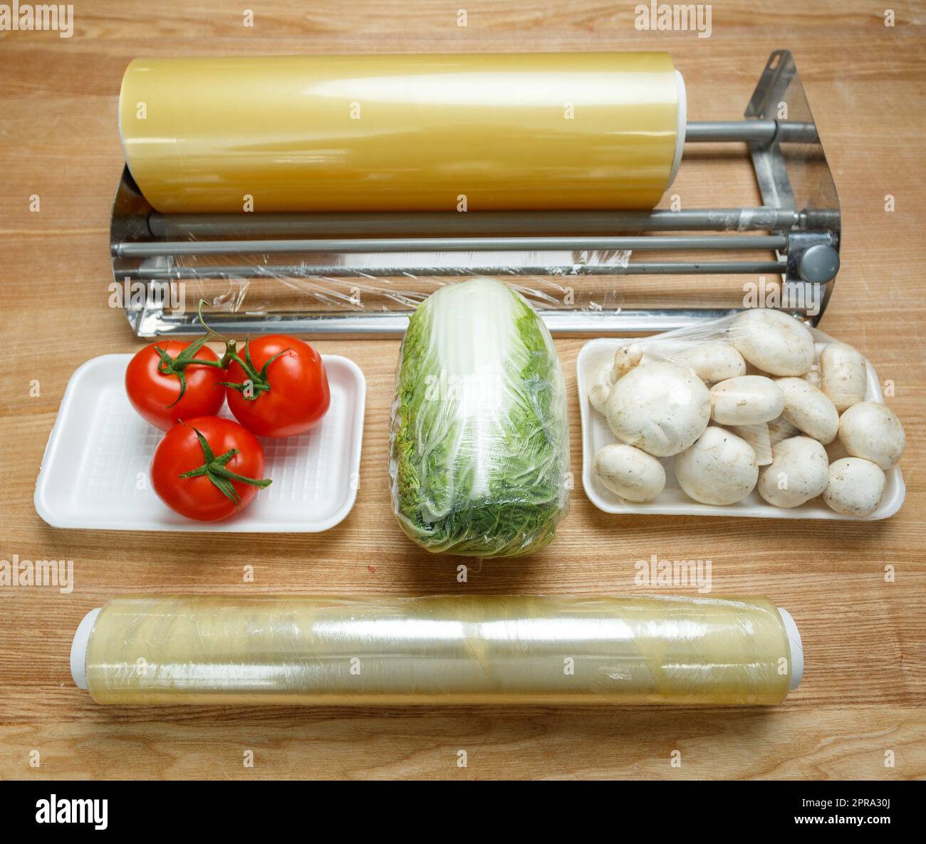 Rollen aus transparenter Polyethylen-Lebensmittelfolie zum Verpacken von Lebensmitteln auf dem Tisch mit Gemüse. Stockfoto