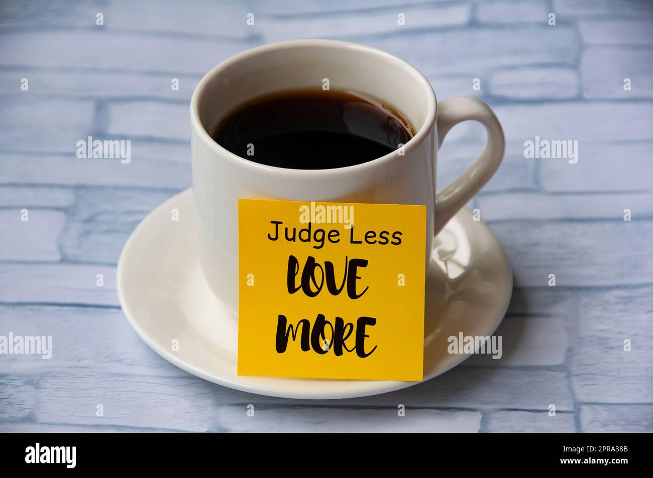 Inspirierender Zitattext auf gelbem Notizblock auf der Kaffeetasse – Judge less love more. Motivationskonzept Stockfoto