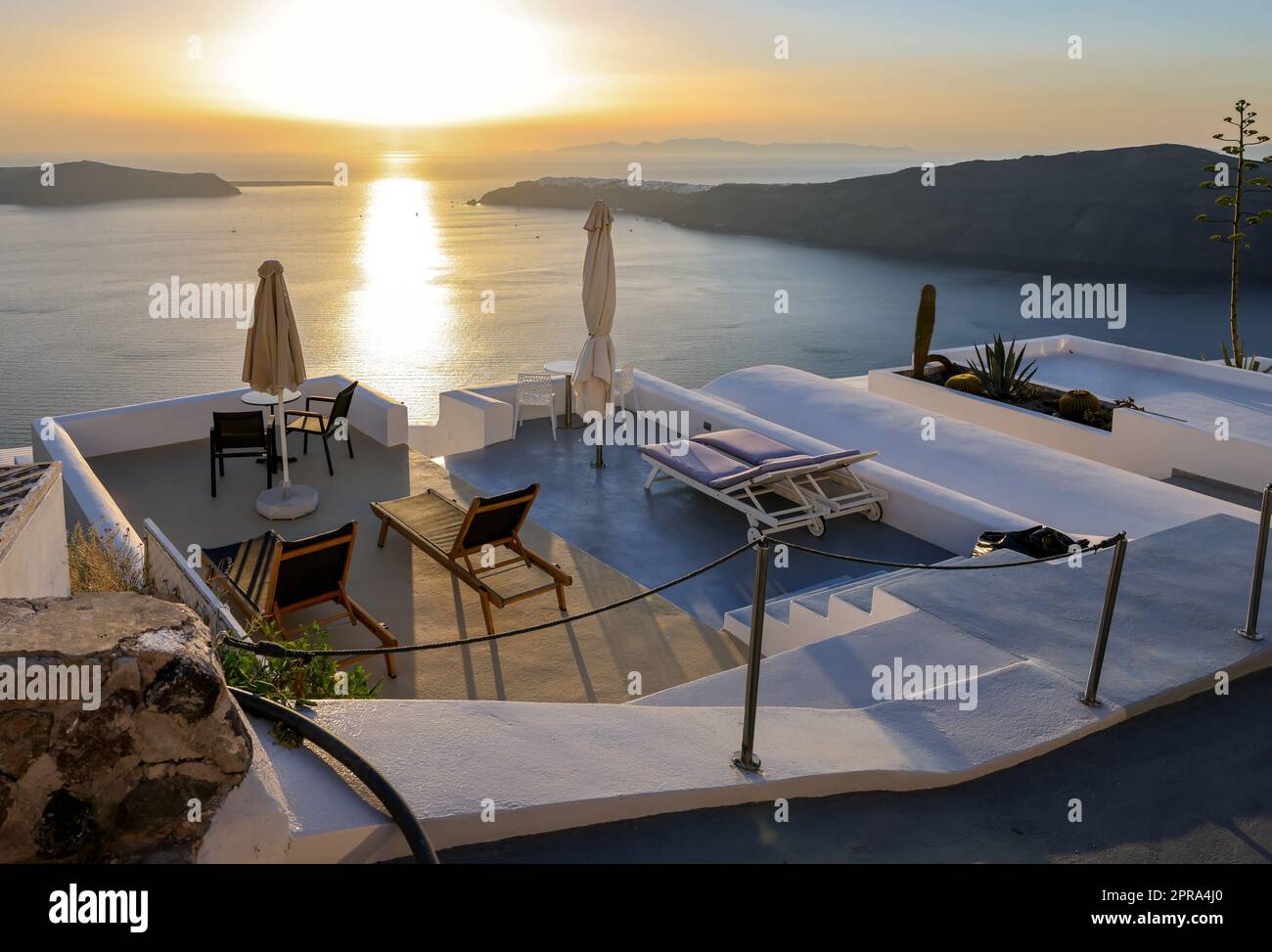 Sonnenliegen auf der Terrasse im Dorf Imerovigli mit herrlichem Blick auf den Sonnenuntergang über der Caldera in Santorin Stockfoto