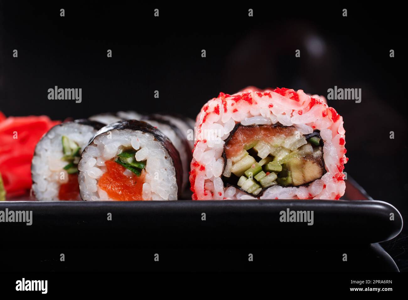 Japanische Reisbrötchen Uramaki und Maki mit Lachs, Gurke und rotem Kaviar auf einem schwarzen Teller. Stockfoto