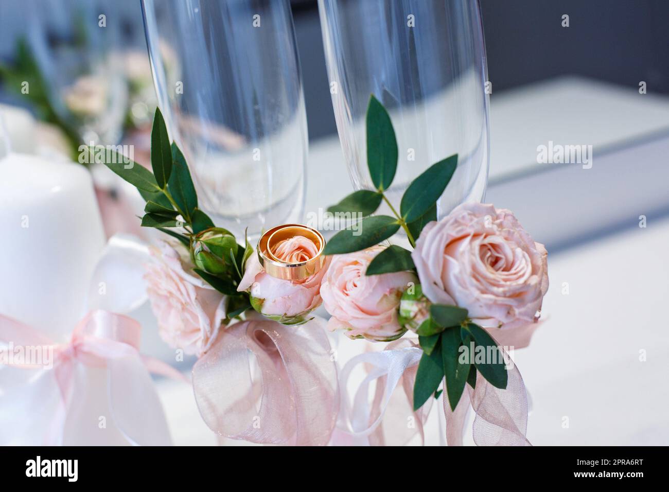 Zwei goldene Eheringe liegen auf Blumen, die Champagnergläser dekorieren. Stockfoto