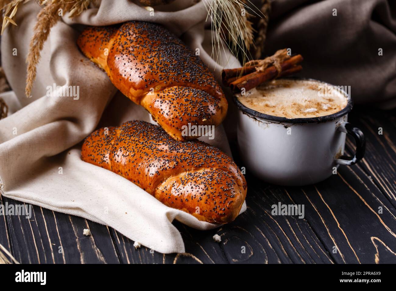 Traditionelles Frühstück mit Mohn-Brötchen und Kaffee auf rustikalem dunklen Holztisch. Stockfoto