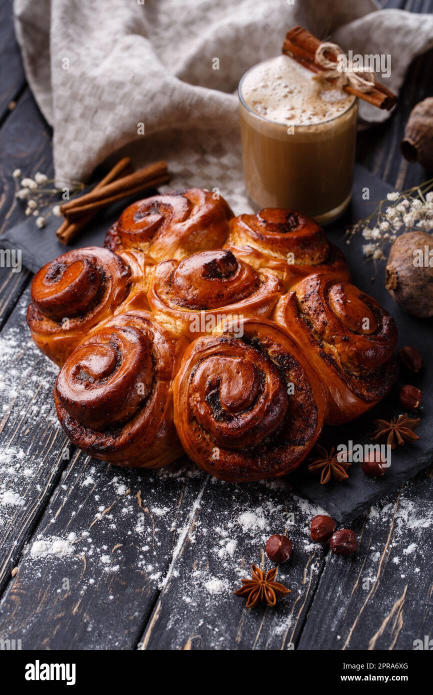 Frisch gebackene Zimtbrötchen mit Gewürzen und Füllung mit Kaffeegetränk auf Holztisch. Stockfoto