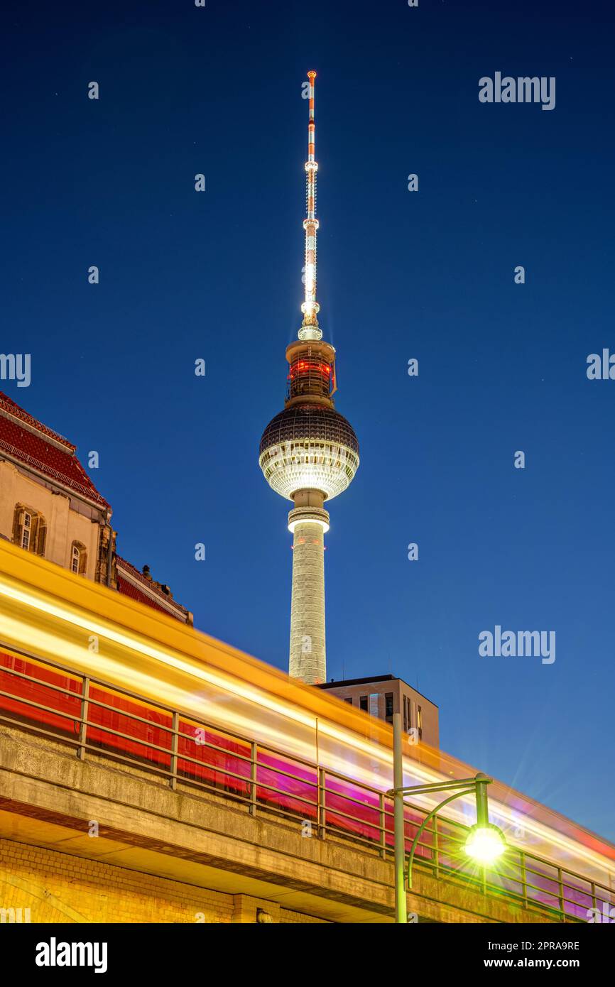 Der berühmte Fernsehturm in Berlin bei Nacht mit einem bewegungsunscharfen Pendlerzug Stockfoto