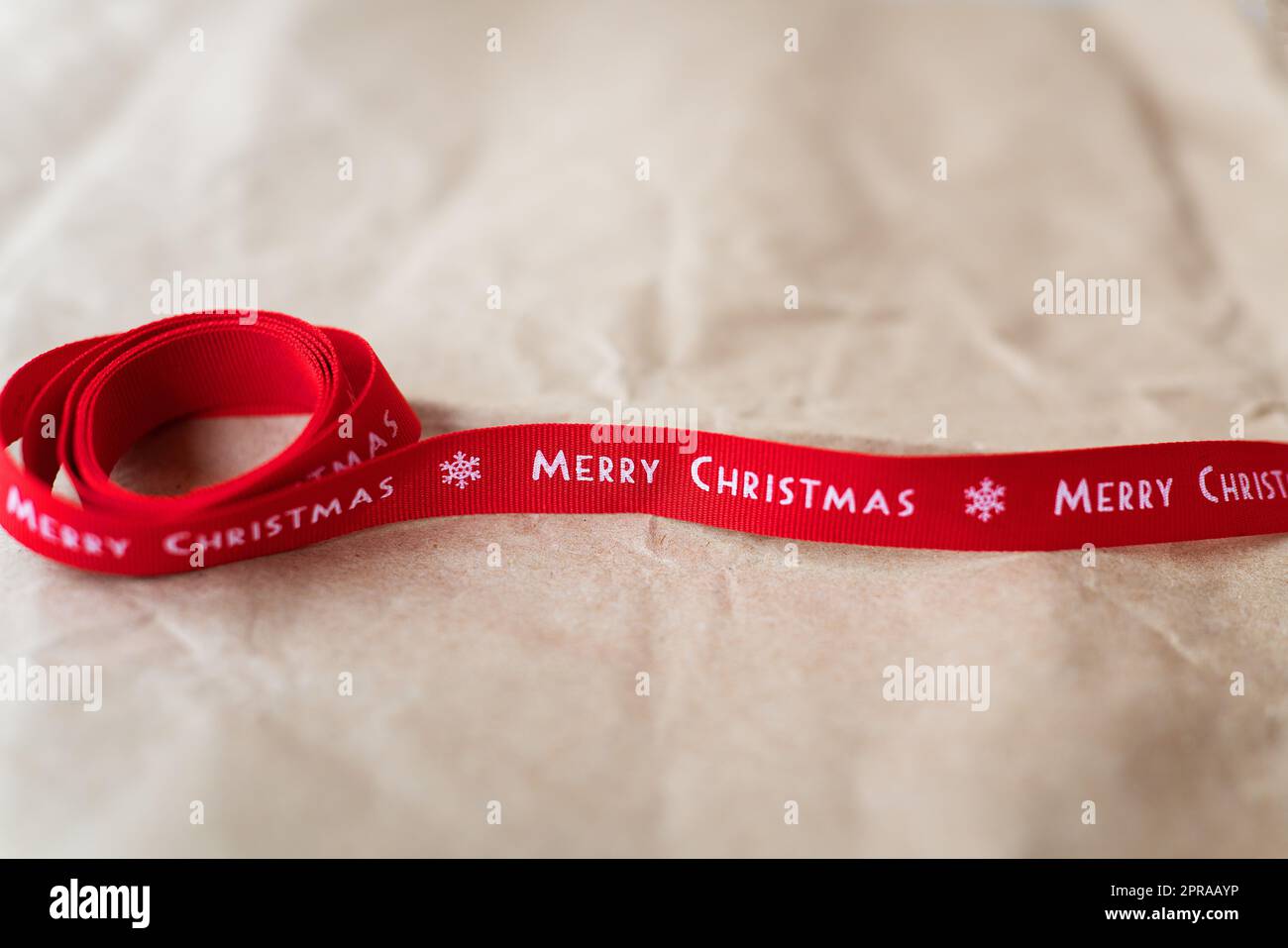 Rotes Band mit der Inschrift Merry Christmas breitet sich auf Handwerkerpapier aus. Platz für eine Inschrift. Stockfoto