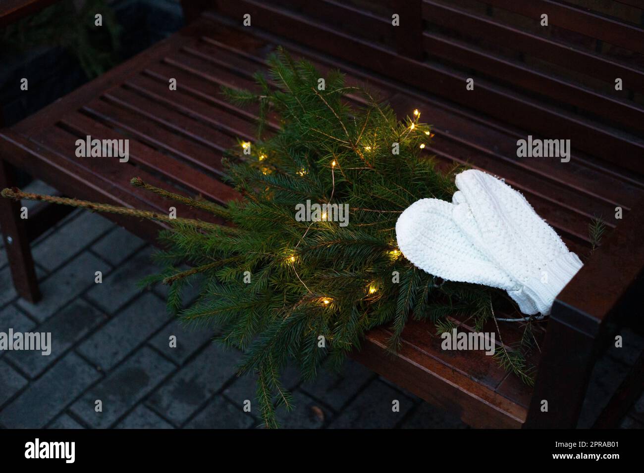 Äste eines Nadelbaums mit Girlande liegen auf einer Bank zusammen mit gestrickten weißen Fäustlingen. Stockfoto