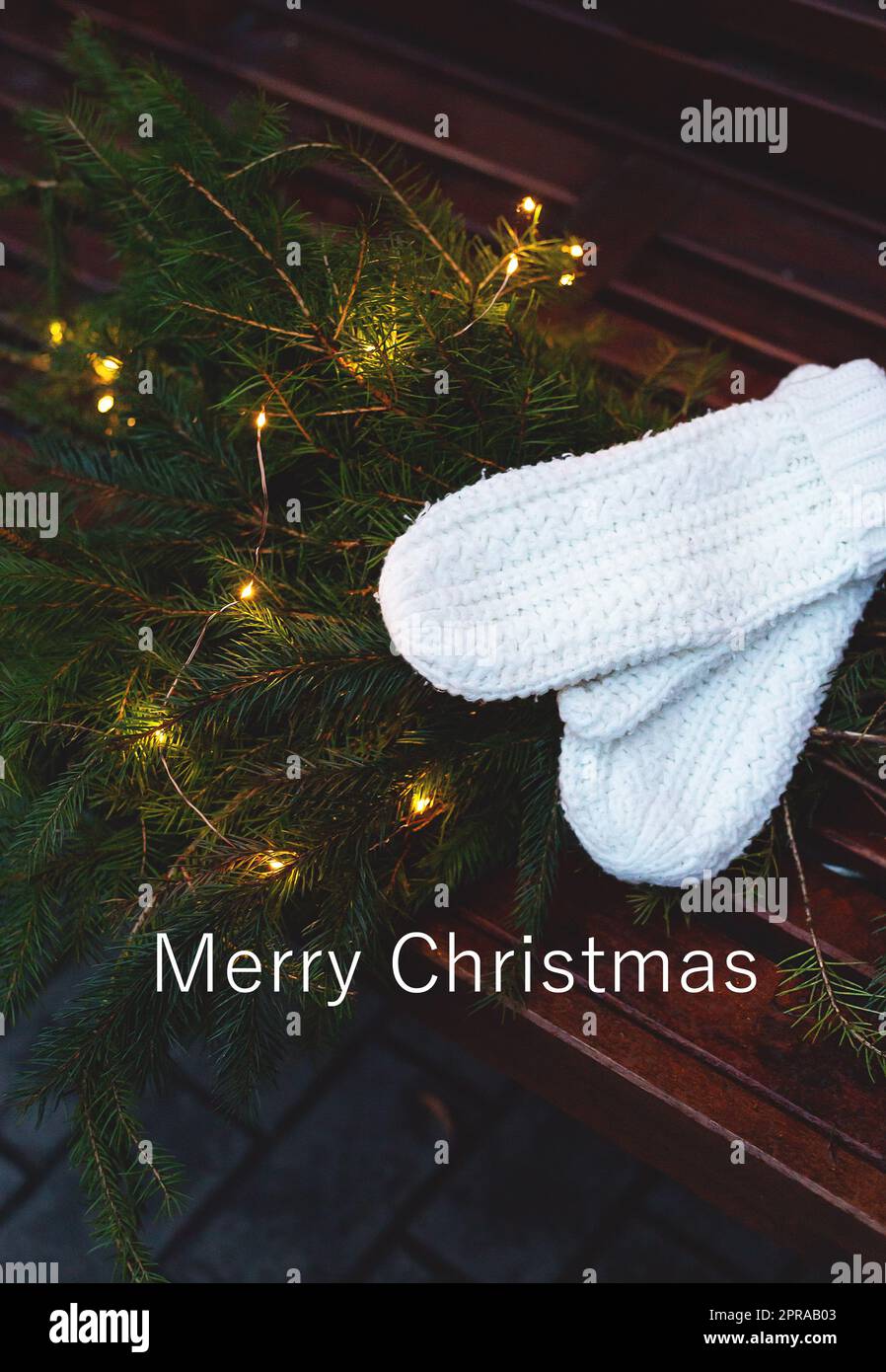 Frohe weihnachtsbriefe. Äste eines Nadelbaums mit Girlande liegen auf einer Bank zusammen mit gestrickten weißen Fäustlingen. Stockfoto