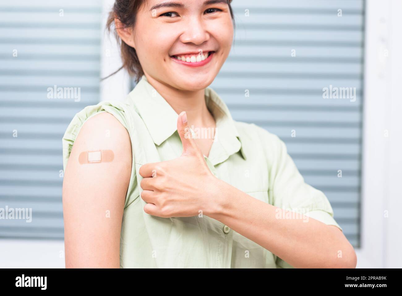 Asiatische junge Frau zeigt gestikulierenden Daumen nach oben oder wie und ihren Arm mit Gipsband Hilfe nach Coronavirus Covid-19 Impfstoffinjektion auf der Schulter, coron Stockfoto