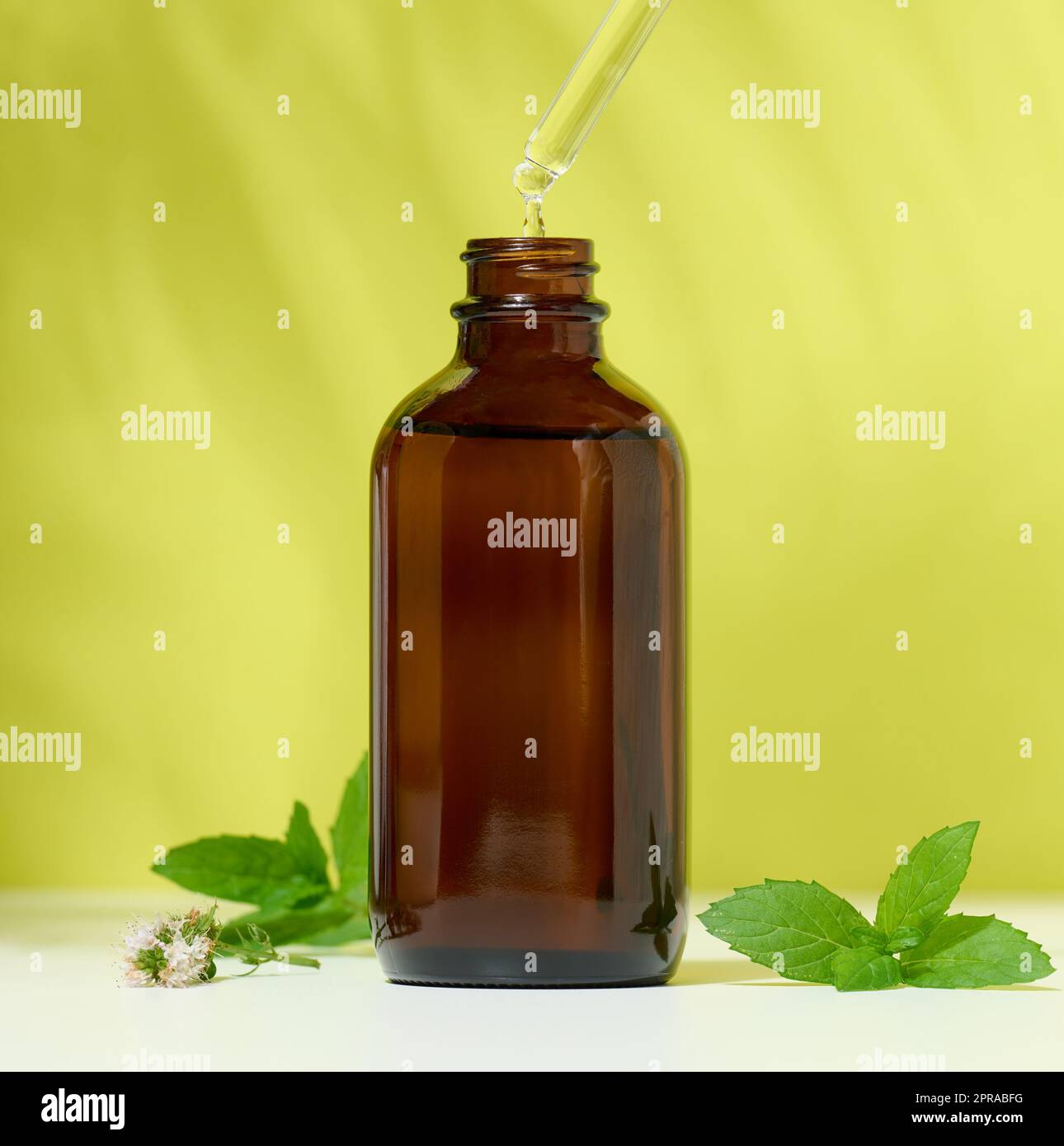 Braune Glasflasche mit einem kosmetischen Mittel und einer Pipette mit einem tropfengrünen Hintergrund. Stockfoto