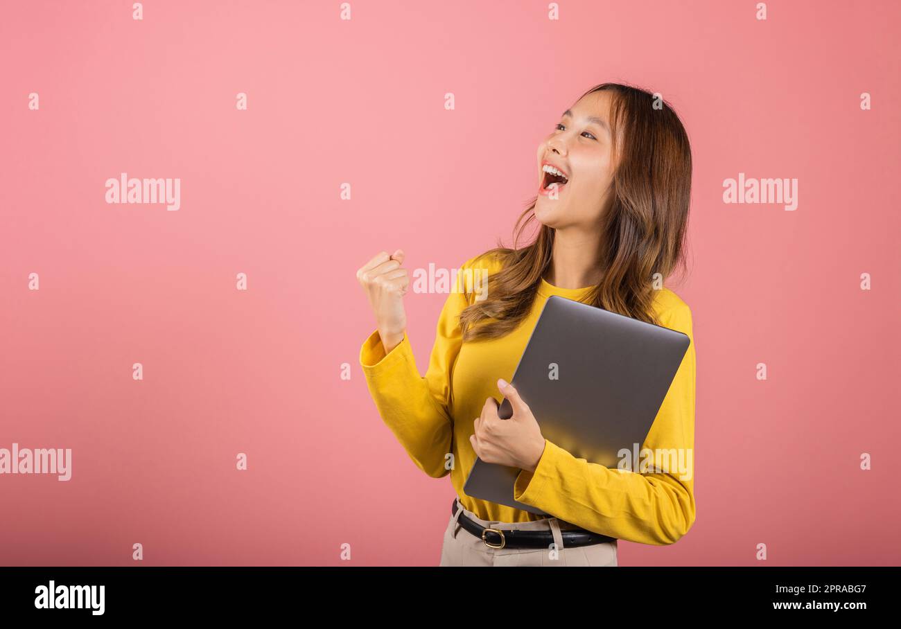 Selbstbewusste Frau, die ein lächelndes Gesicht hält und einen Laptop hält, hebt die Hand und sagt Ja Stockfoto