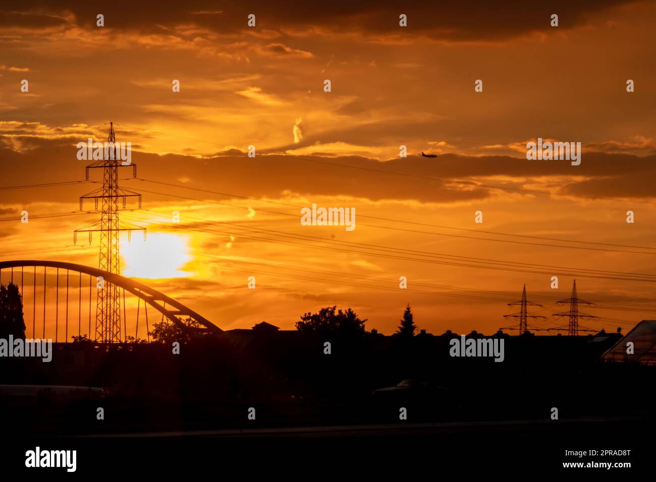 Der goldene Himmel mit Sonnenstrahlen und Linsenerscheinungen zeigt Solarenergie mit der Pylonsilhouette des Stromturms in goldenem Sonnenuntergang und orangefarbenem Himmel für nachhaltige Energie oder erneuerbare Ressourcen von der Dämmerung bis zur Dämmerung Stockfoto