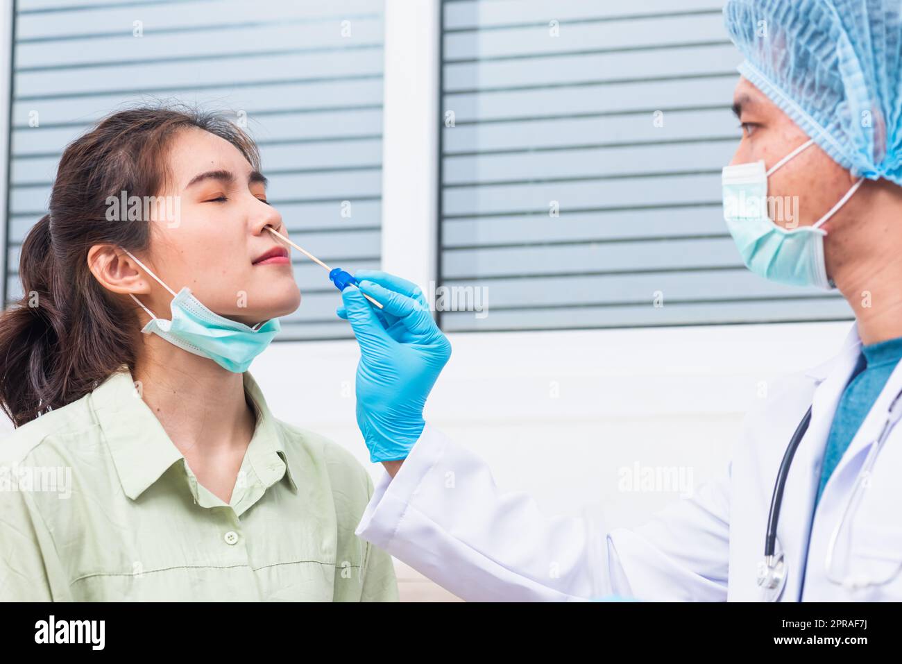 Doktor man nehmen Speichelprobe durch die Nase mit Wattestäbchen, um Coronavirus-Test von einer jungen asiatischen Frau zu überprüfen Stockfoto