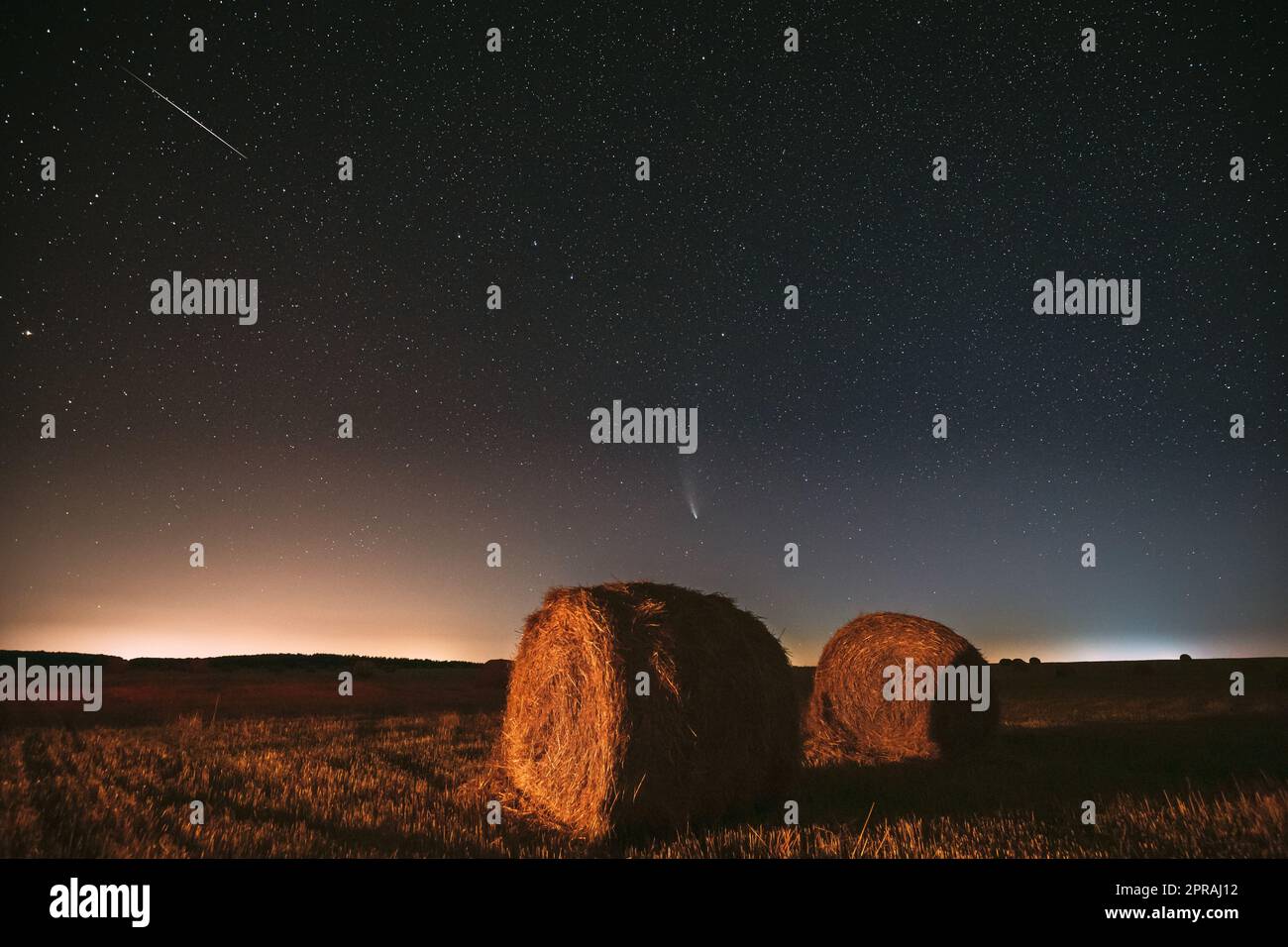 Meteor und Comet Neowise C2020 F3 in Night Starry Sky über Heuhaufen auf dem landwirtschaftlichen Sommerfeld. Nachtstars Über Der Ländlichen Landschaft Mit Heuballen Nach Der Ernte Stockfoto