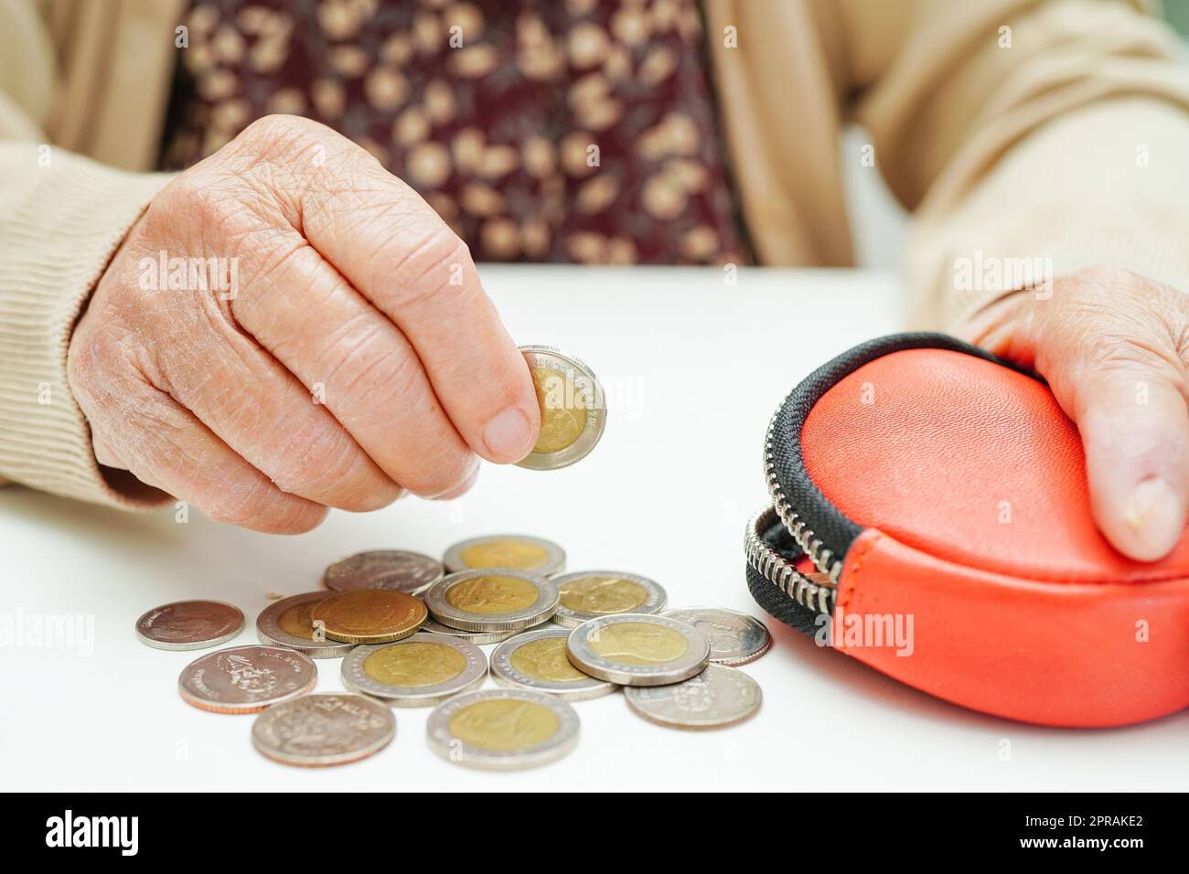 Ältere Frau im Ruhestand, die Münzen zählt, Geld zählt und sich um monatliche Ausgaben und die Zahlung von Behandlungsgebühren sorgt. Stockfoto