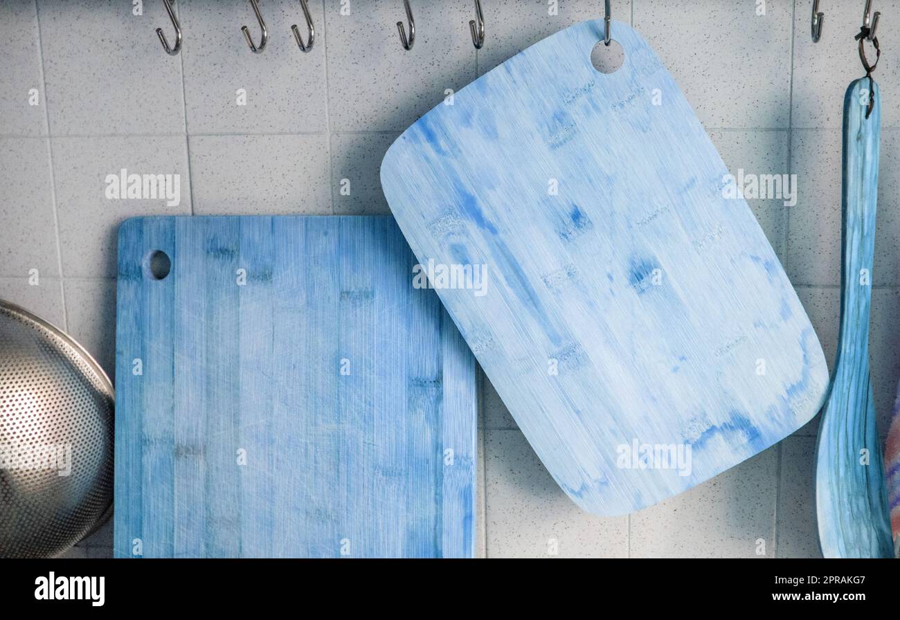 Nahaufnahme von zwei Holzschneidebrettern, die an einer gefliesten Wand an Metallhaken hängen, blau getönt Stockfoto