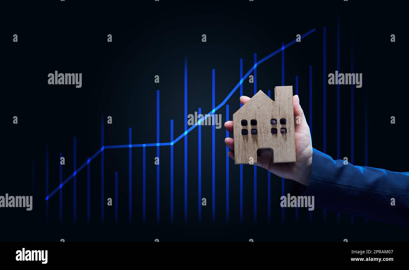Die Hand hält ein hölzernes Modell eines Hauses auf dunklem Hintergrund. Immobilienverkauf Stockfoto