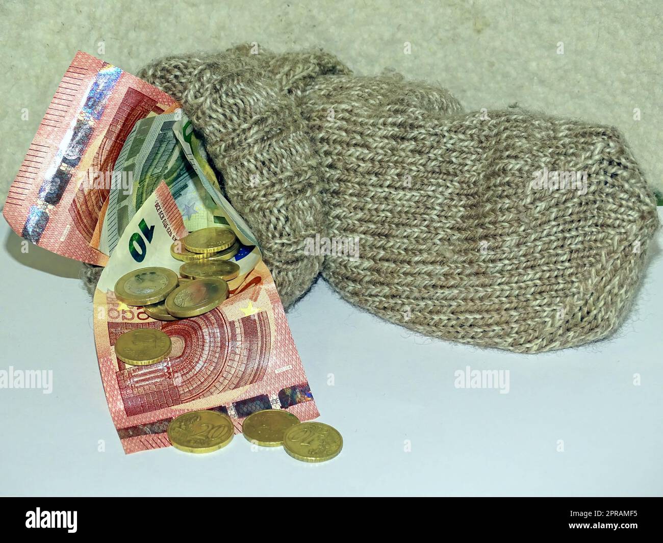 Banknoten und Münzen in Euro in einer gestrickten Wollsocke, die als Ersatzstrumpf verwendet wurde. Stockfoto