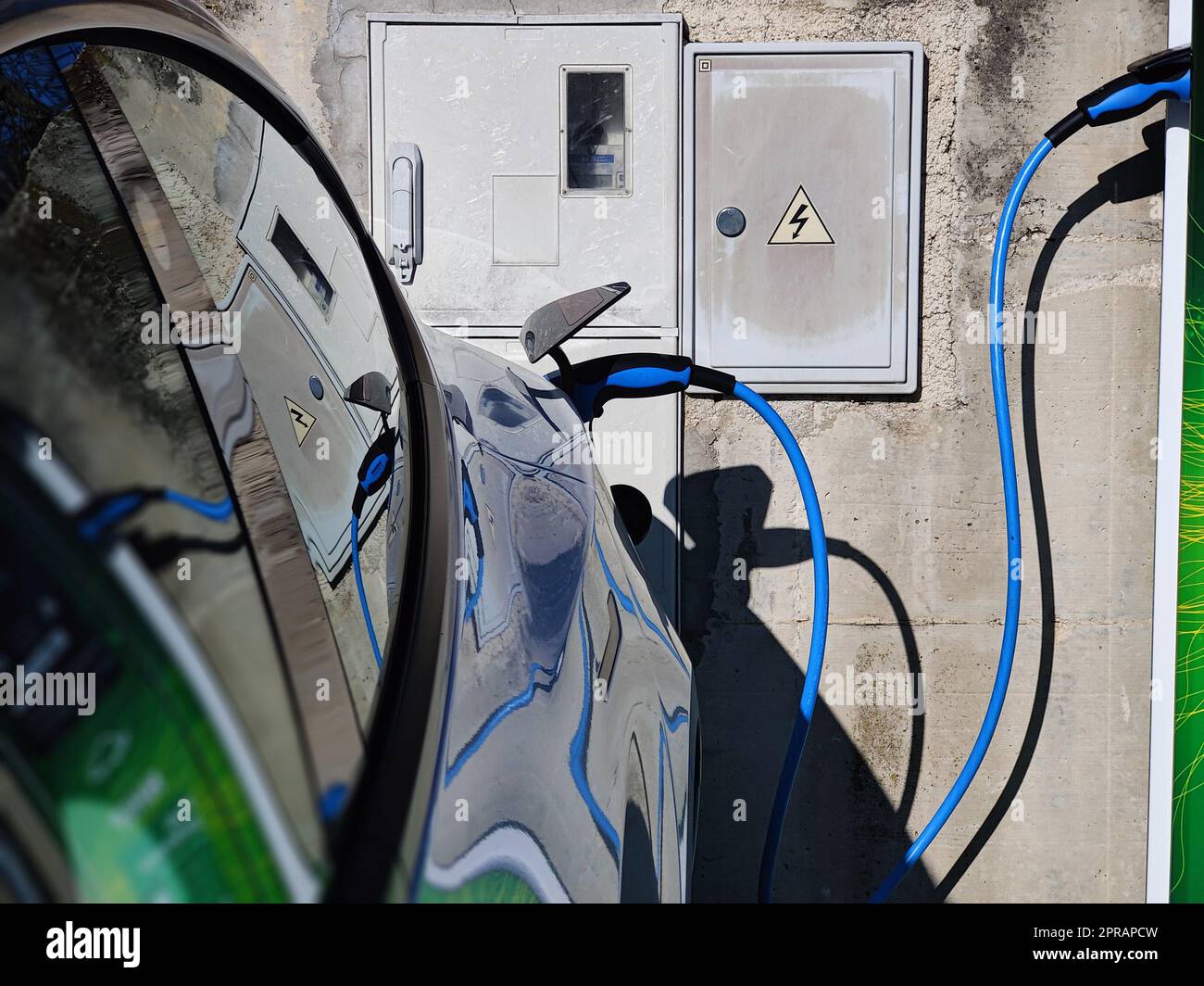 Elektrofahrzeug oder Elektrofahrzeug an der Ladestation mit angeschlossenem Netzkabel auf verschwommener Natur mit blauem Enegy Power-Effekt. Umweltfreundliches Konzept für nachhaltige Energie. Stockfoto