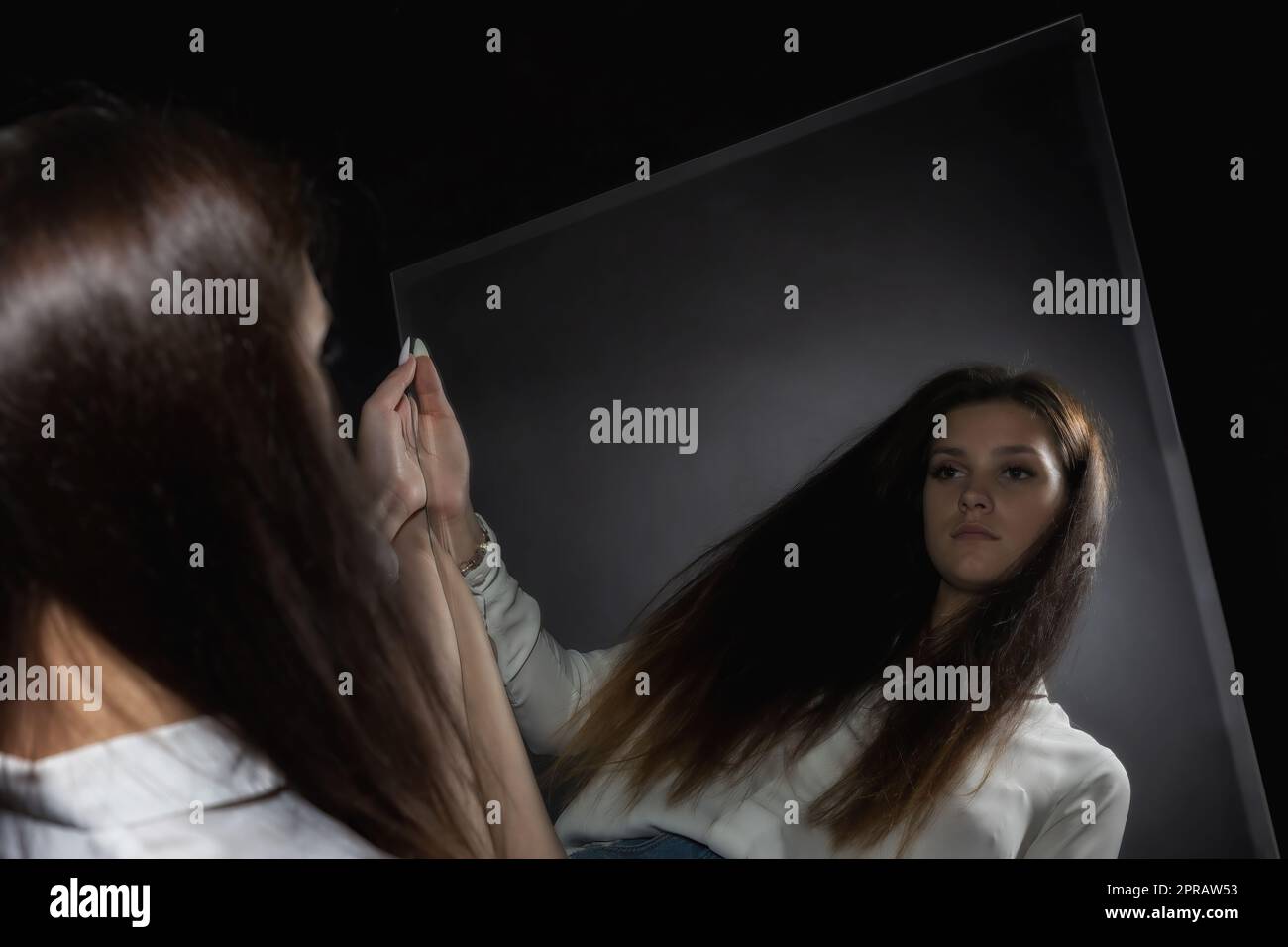 Eine junge Frau, die ihr Spiegelbild im Spiegel betrachtet. Stockfoto