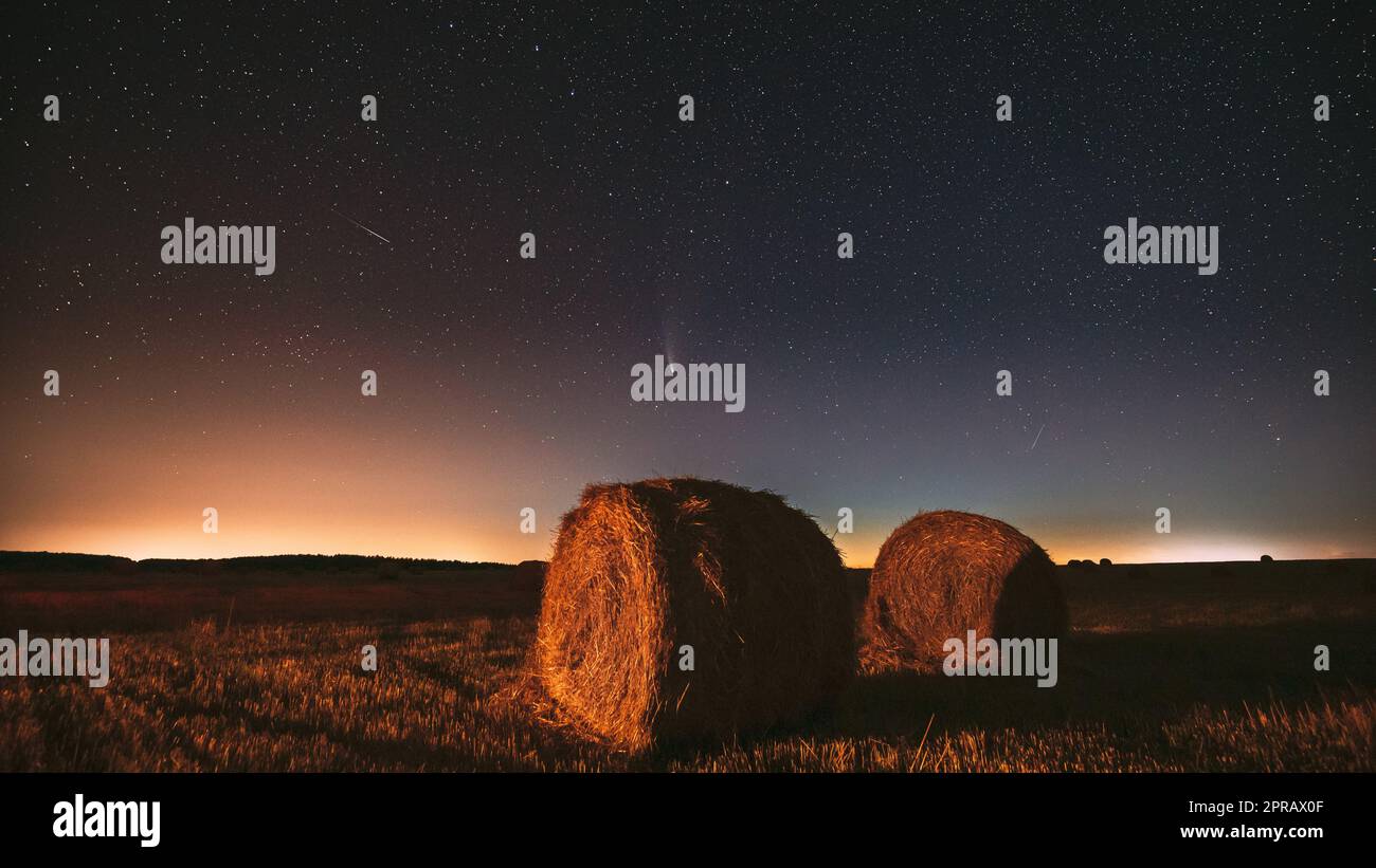 Meteor und Comet Neowise C2020 F3 in Night Starry Sky über Heuhaufen auf dem landwirtschaftlichen Sommerfeld. Nachtstars Über Der Ländlichen Landschaft Mit Heuballen Nach Der Ernte Stockfoto