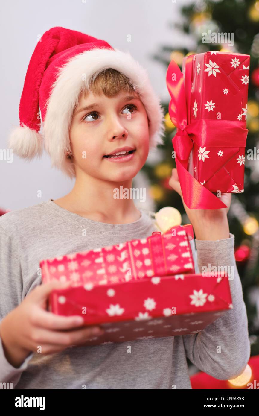 Porträt eines neugierigen Kindes, das am Weihnachtsmorgen am Weihnachtsbaum Geschenke hält. Stockfoto