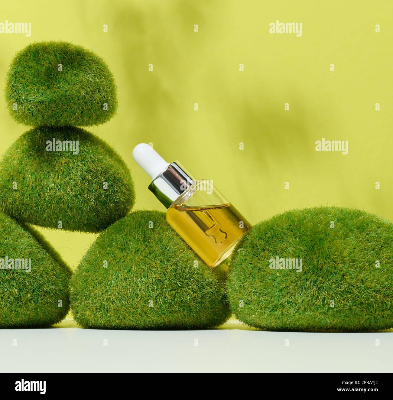 Transparente Glasflasche mit Pipette und gelbem Öl auf grünem Moos. Stockfoto