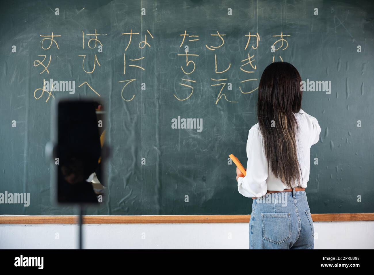 Asiatische Lehrer unterrichten an Bord, während sie online über Smartphone im Klassenzimmer Tafel-Vorlesungen halten Stockfoto