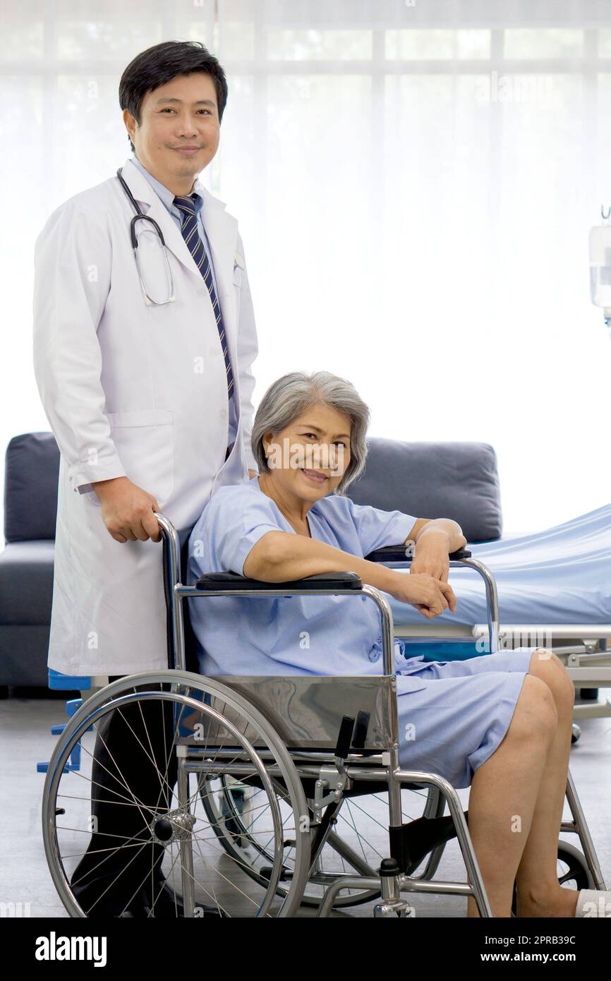 Portrait eines asiatischen Arztes mit Stethoskop und Kittel schieben einen Rollstuhl des älteren Patienten. Gesundheits- und Medizinkonzept. Stockfoto
