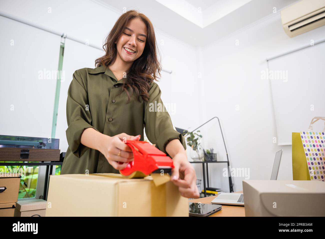 Asiatische junge Frau, die eine Handpackung mit Transparentband im Heimbüro macht Stockfoto