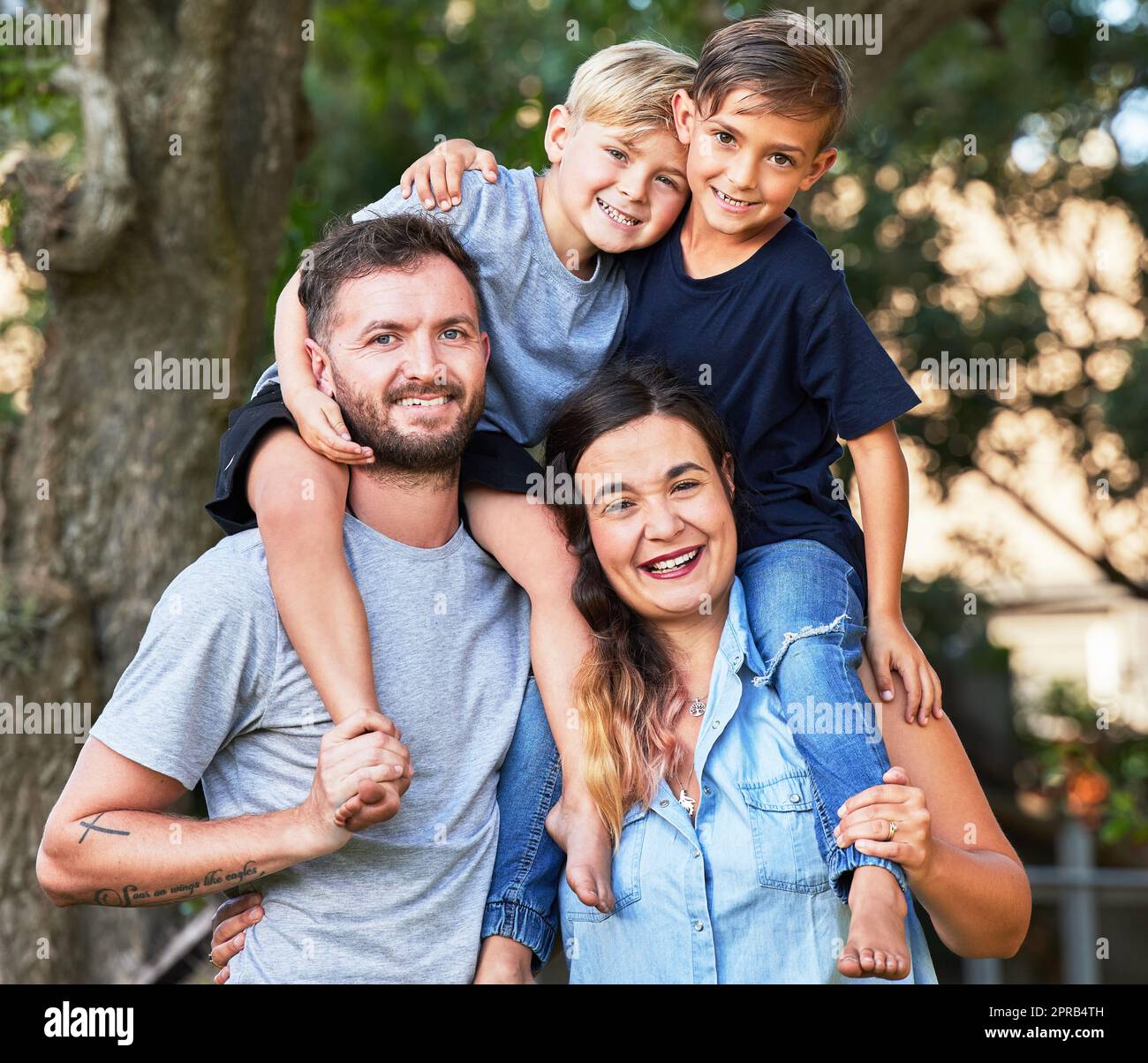 Kind, das mit Sicherheit lebt, lernt, Glauben zu haben. Porträt einer schönen Familie mit ihren Söhnen auf den Schultern in einem Park. Stockfoto