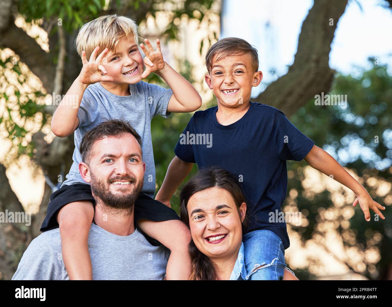 Vater – jemand, der Bilder trägt, wo er einst Geld aufbewahrt hat. Porträt einer schönen Familie mit ihren Söhnen auf den Schultern in einem Park. Stockfoto