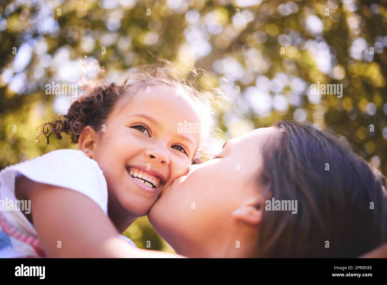 Ich verbringe gerne Zeit draußen mit dir. Eine junge Mutter küsst ihre Tochter liebevoll auf die Wange. Stockfoto