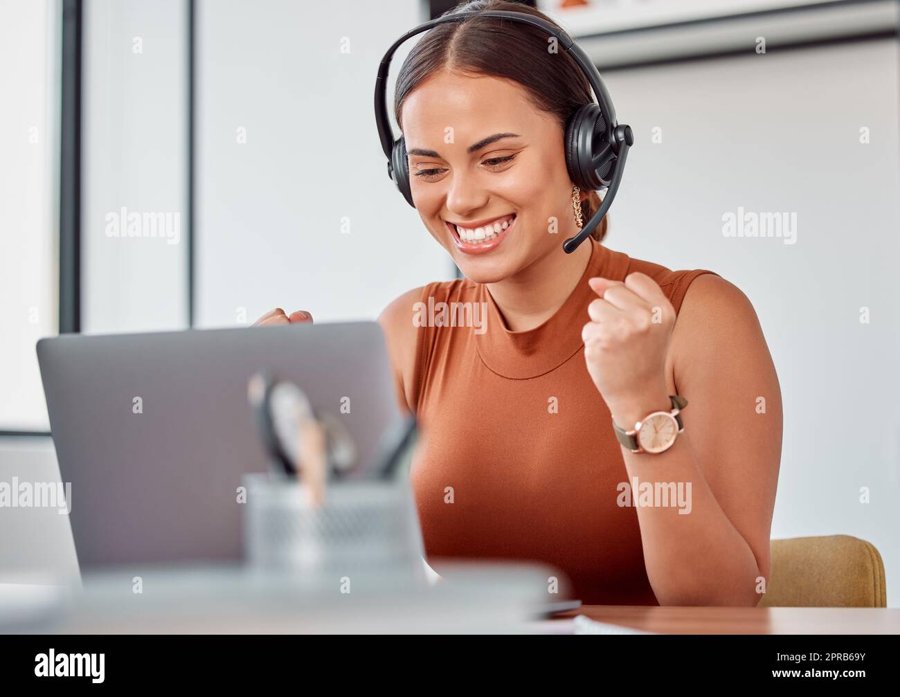 Ja, eine weitere glückliche Kundin. Eine attraktive junge Callcenter-Agentin jubelt, während sie an ihrem Laptop arbeitet. Stockfoto