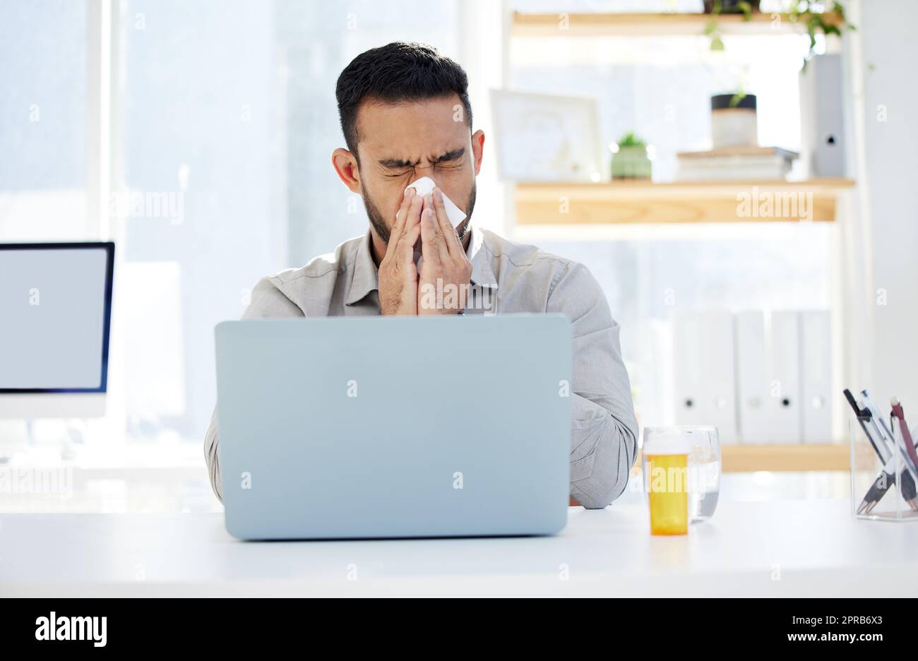 Es ist die Saison zu rotzig sein. Ein junger Mann bläst seine Nase bei der Arbeit in einem modernen Büro. Stockfoto