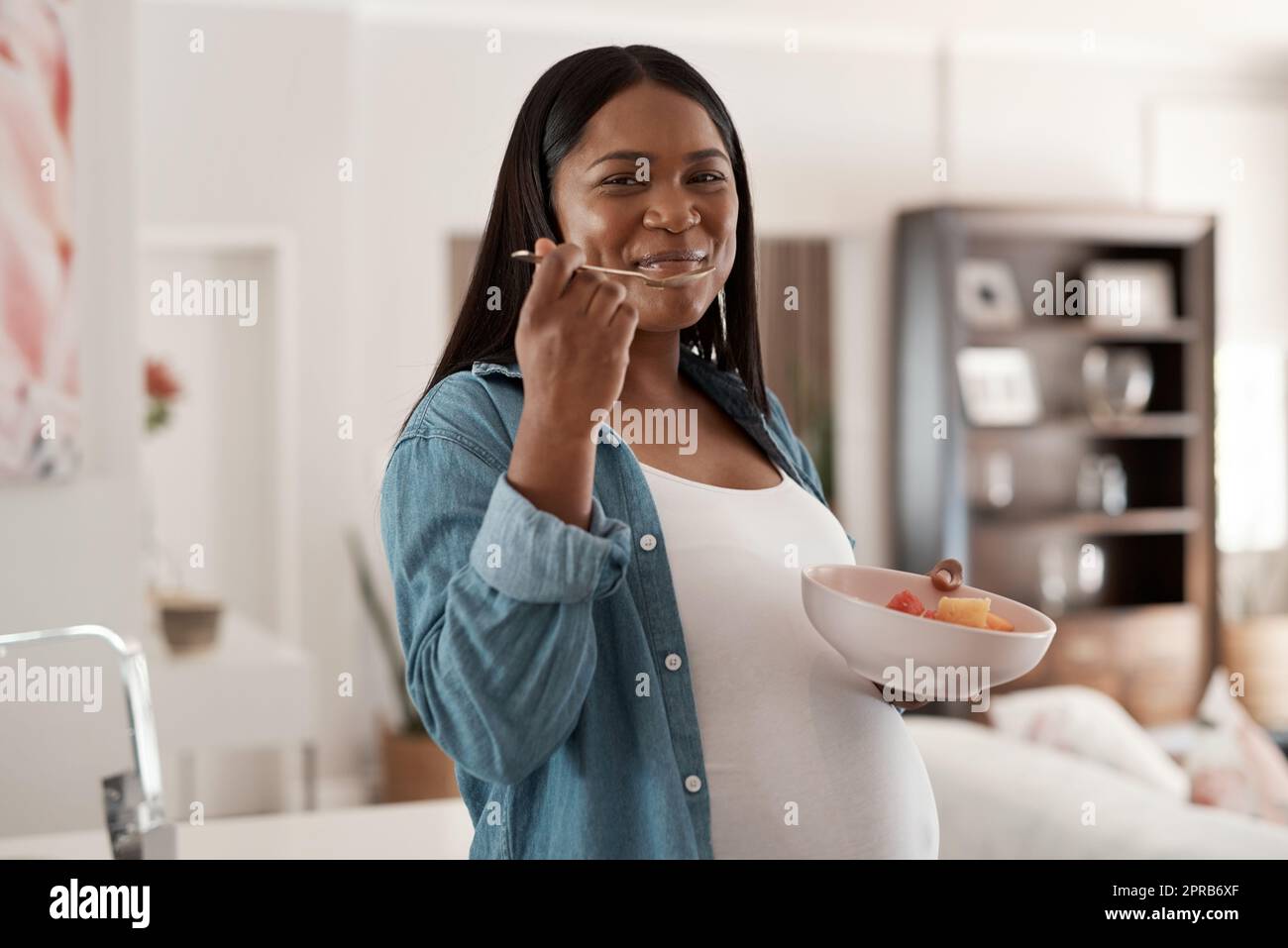 Mama und Baby müssen auch gesund essen. Porträt einer Schwangeren, die zu Hause eine Schale mit Obst isst. Stockfoto