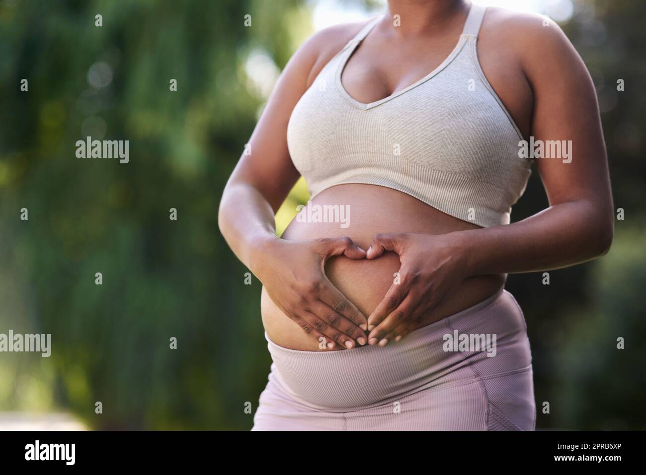 Meine Liebe zu Ihnen ist es, was mich motiviert, gesunde Entscheidungen zu treffen. Eine Frau, die eine Herzform auf ihrem schwanger Bauch bildet. Stockfoto