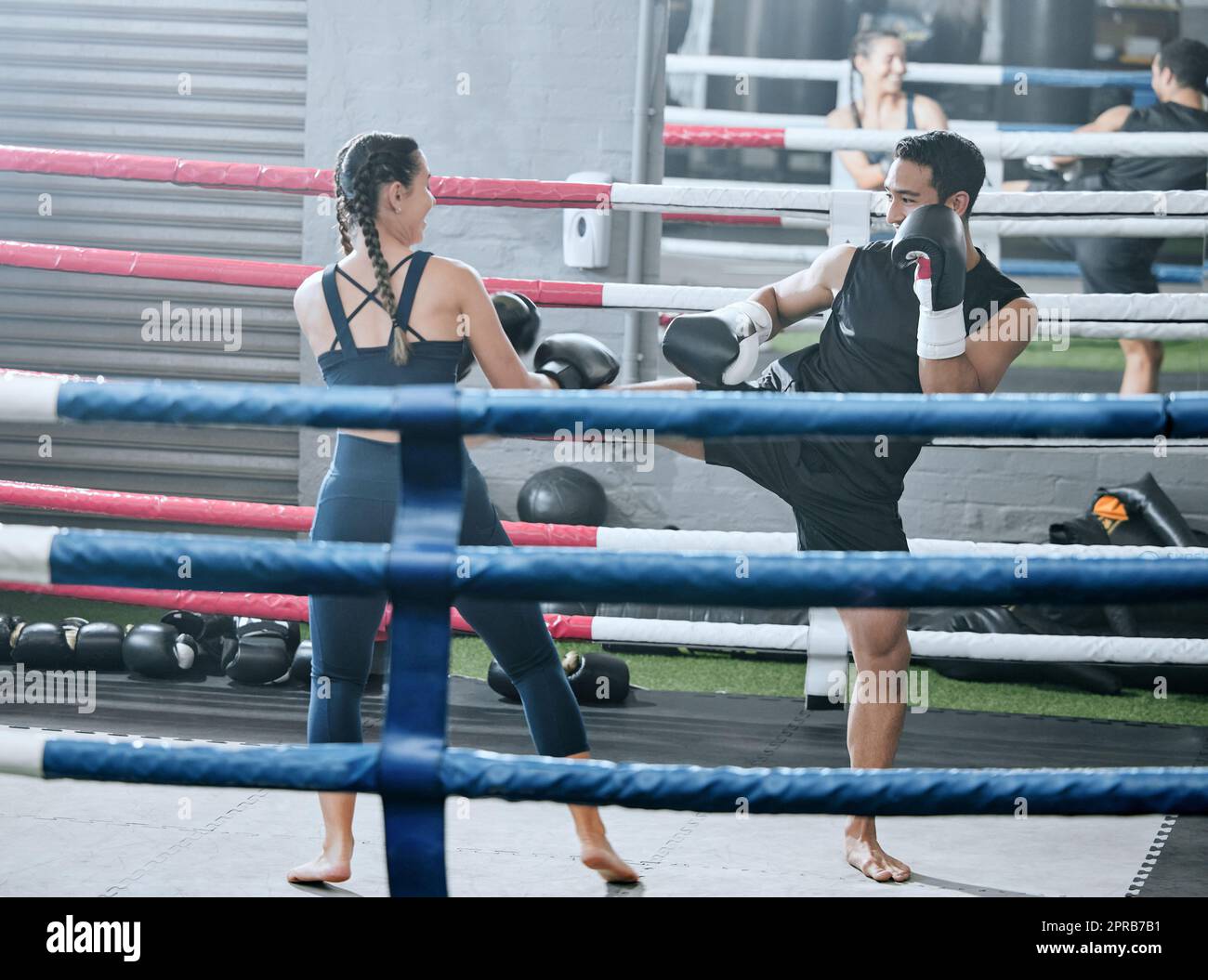 Fit, gesund und aktiv Frau macht Kickboxing Workout im Gym Sparring mit ihrem Personal Trainer in einem Wellnesscenter lernen zu kämpfen. Sportlicher Mann gegen Frau in einem Boxsport-Spiel in einem Ring Stockfoto